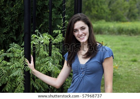 Young woman smiling beside a black wrought iron fence in a nature area