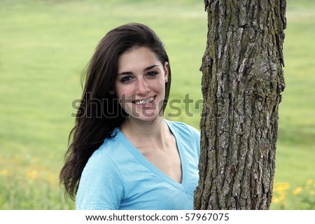 Young woman smiling beside a tree in a meadow area