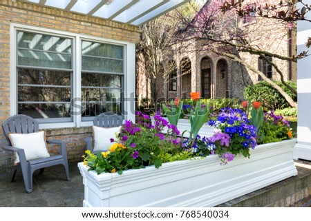 Variety of flowers in a flower pot with deck chairs on a front porch of a suburban home.