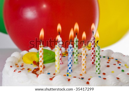 Birthday cake with lighted candles and balloons.