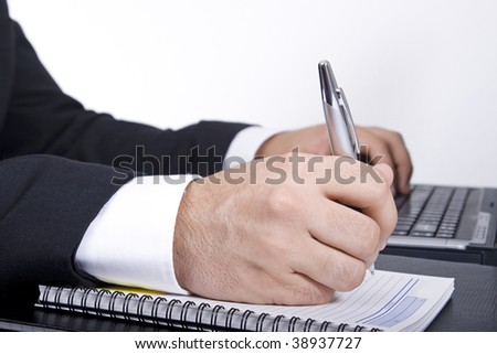 Business man writing on a message pad and typing with the other hand.