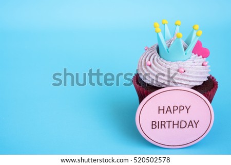Happy birthday cupcake with crown and pink heart over blue background with copy space