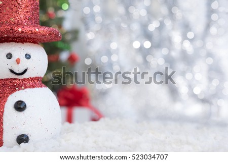 Snowman on snow over blurred christmas tree and gift box on glitter light bokeh background with copy space