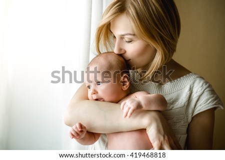 newborn baby in a tender embrace of mother at the window. mother holding a small child in the window