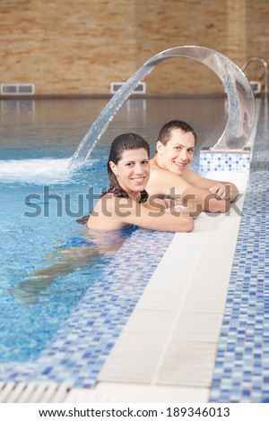 Smiling man and woman in swimming pool against background of spa hydrotherapy waterfall