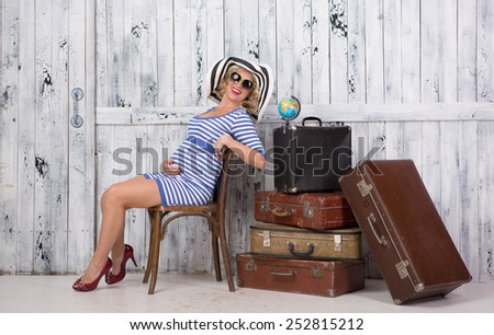 Stylish pregnant lady tourist with suitcases near wooden wall