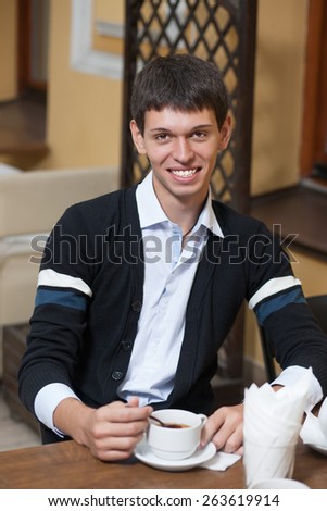 He is positive handsome. Young man posing for camera across table with cup of coffee