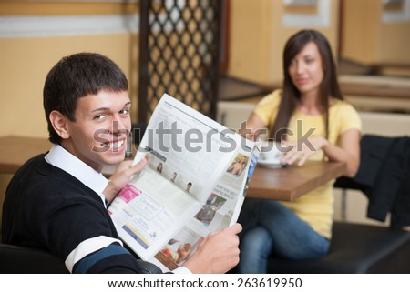 Read news and drink coffee. Young beautiful man posing across table with cup of coffee