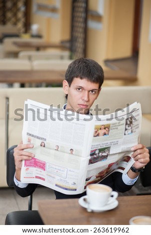 He serious man and he read newspaper. Young beautiful man posing across table with cup of coffee