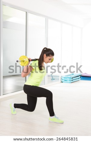 Beautiful sporty woman in yellow t-shirt make sit with barbell in gym