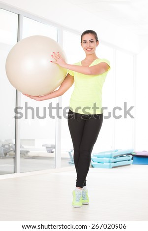 She stay with pilates ball in gym and going to make exercise.