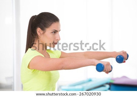 Sports woman hold dumbbells in double arms. Beautiful woman in yellow t-shirt in sport gym.