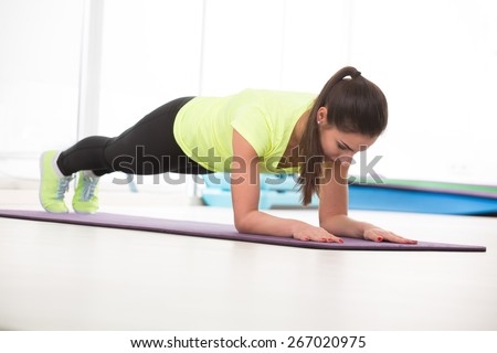 Beautiful woman do push ups in sport gym in yellow t-shirt on floor.