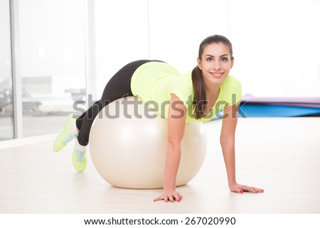 Sporty woman works in sportgym with fitness ball. Beautiful woman in yellow t-shirt and black  jogging trousers posing for camera.