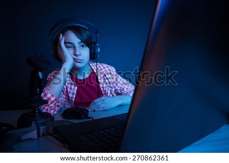 Bored boy. He want ot sleep after video games played all night long. In blue light of display emotional kid play computer games online.
