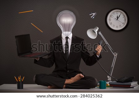The businessman generating ideas in office, while his work is doing. Handsome businessman sit on table in office in lotus position with head in shape of electric lamp.