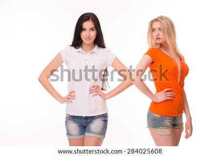 Sexy girls with arms akimbo posing for photographer. Girls standing in white and orange T-shirts on white background.