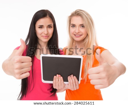 Sexy girl in orange T-shirt showing OK sign. Sexy girl in pink T-shirt looking at tablet PC.