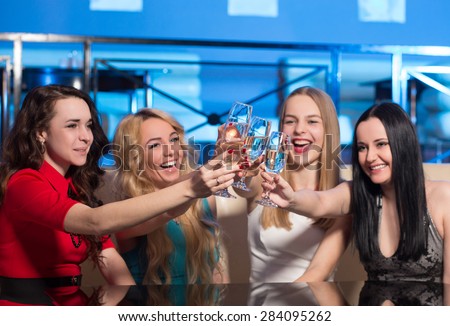 Young friends clanging glasses with sparkling wine. Blonde, brunette and chestnut girls in clubbing wearing satisfied by their happy evening in nightclub.