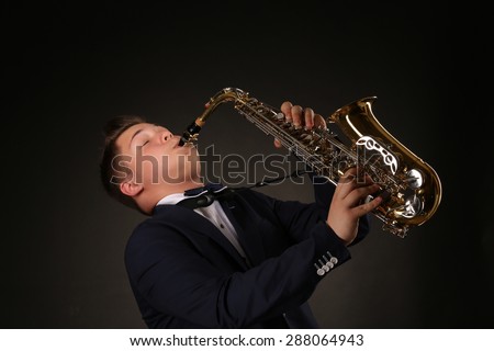 Photo of a teenager playing the saxophone. Man in navy blue suit performing on dark background.