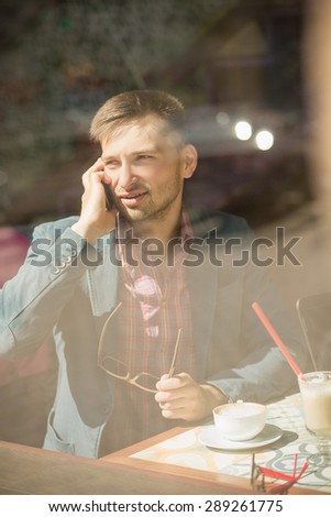 Cute tartupper calling to bank. Man in casual suit sitting in restaurant with a cup of capuccino.