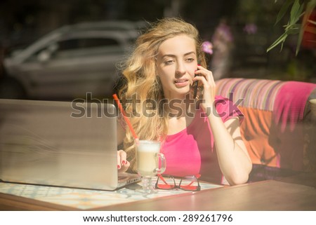 Beautiful and serious woman working with her phone and laptop in restaurant. Girl drinking a cup of coffee.