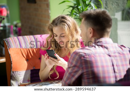 Man and woman having date in restaurant. Sexy girl in pink T-shirt using Internet all the time.