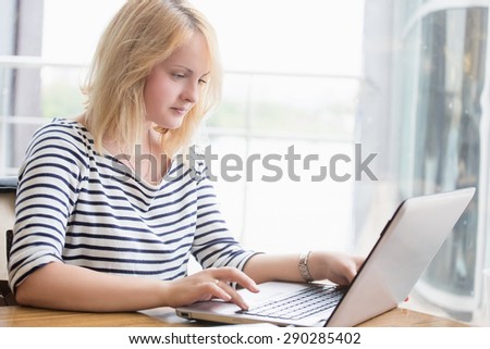Woman using laptop indoors. Happy young beautiful girl in sailor suit typing messages to her friends.