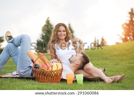Happy couple enjoying picnic. People having rest with much food, drinks. Girl smiling to camera.