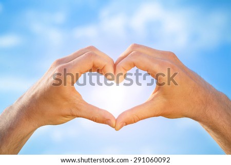 Male hands in the form of heart isolated on blue sky background. Sun is shining.