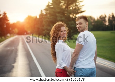 Happy couple holding hands in the sunset. Man and woman in white T-shirts smiling.
