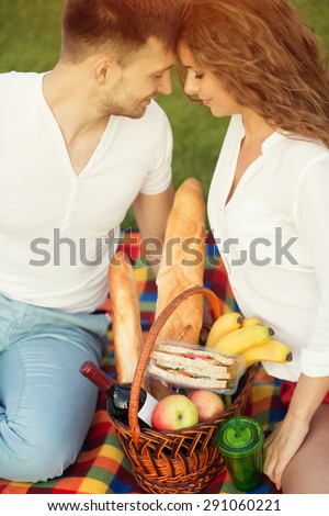 Beautiful young couple in love. Man and woman sitting on the carpet full of food and drinks face to face.