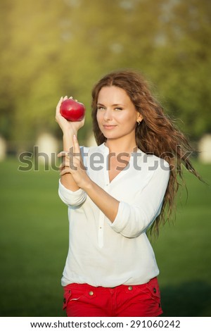 Woman with apple posing for photographer. Long-haired girl holding red apple in her hand.
