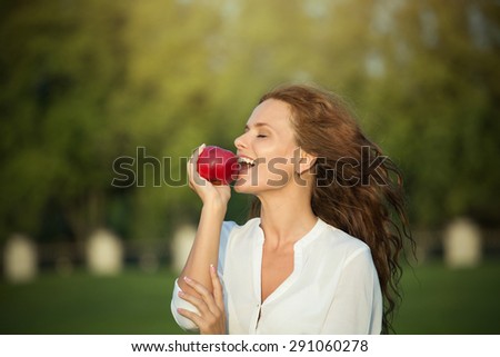 Portrait of woman eating apple. Smiling lady going to to eat red-coloured apple in the sunset.