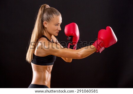Active boxing woman jumping high on black background. Brown-haired woman with red boxing gloves posing.