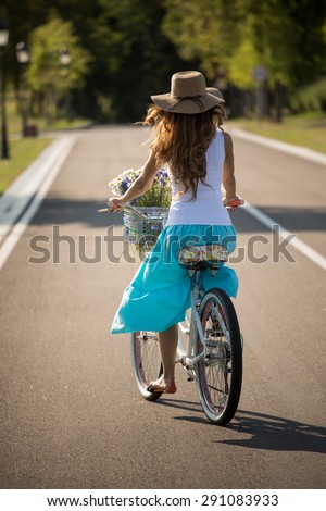 Profile of summer girl on a bicycle. Girl with straw hat on using vehicle full of beautiful flowers.