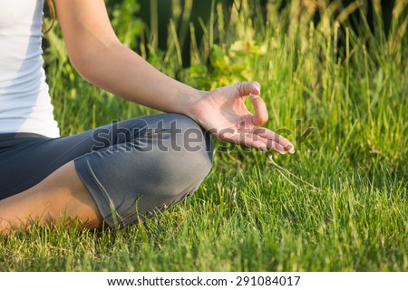 Portrait of serene young woman. Girl in white singlet sitting cross-legged and meditating with her fingers in yogic.