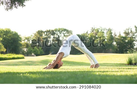 Sporty yogi girl stretching in pose Adho Mukha Svanasana. Girl in white sports suit training in the air.