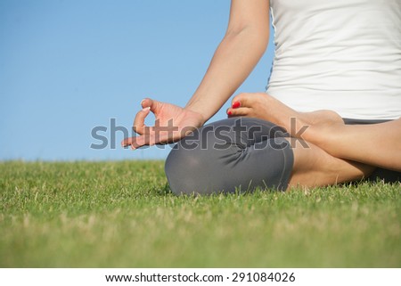 Pretty young woman practicing yoga on the grass. Yoga girl in white singlet sitting in lotus pose.
