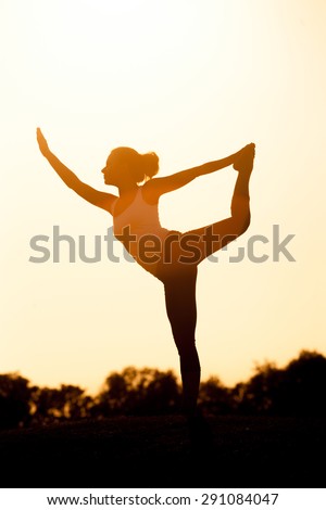 Girl silhouette exercising yoga. Woman in sport suit training in the sunset.