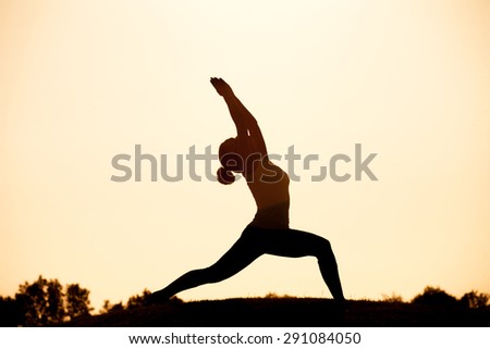 Black  silhouette of yogi girl in low lunge pose - asana pose. Beautiful woman practicing outdoors against sunset sky.