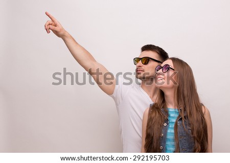 Young couple looking at the blue sky. Man and woman in sunglasses happy smiling on grey background.