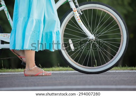 Close-up of summer girl with bicycle. Woman in blue skirt standing near bicycle on the road.