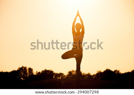Yogi girl in asana pose. Silhouette of woman practicing yoga pose standing in the lotus position with her hands raised against a colorful sunset sky.