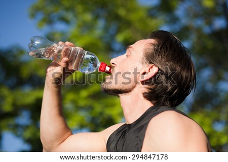 Handsome man drinking fresh water from bottle. Caucasian jogger man drinking water under the blue sky outdoors.
