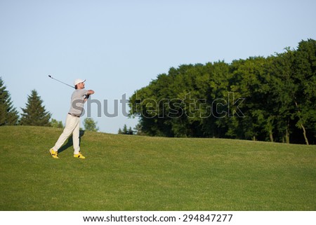 Man with hat on playing professional golf in the air. Golfer hitting golf shot with club on the course.