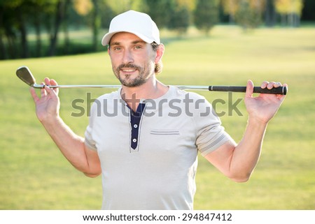 Man holding a golf club and stretching his back. Handsome young professional golf player T-shirt isolated on green.