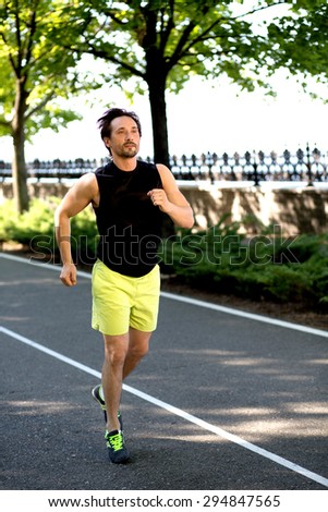 Sporty fit young man jogging. Man in black singlet and yellow shorts training for healthy lifestyle in the park.