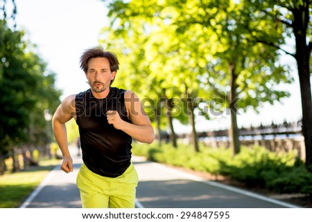 Handsome man running outdoors at full speed. Sexy brunette in sports clothes dreaming abour getting perfect body.