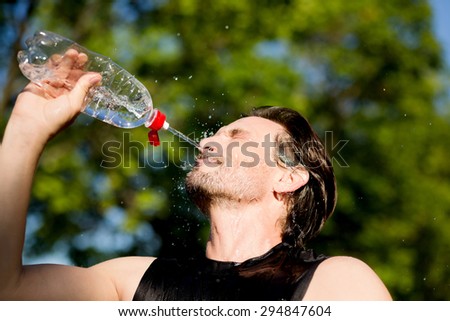 Sporty man refreshing with cold water after run training work out in the park. Sport fitness young happy model taking a break after jogging in the nature.
